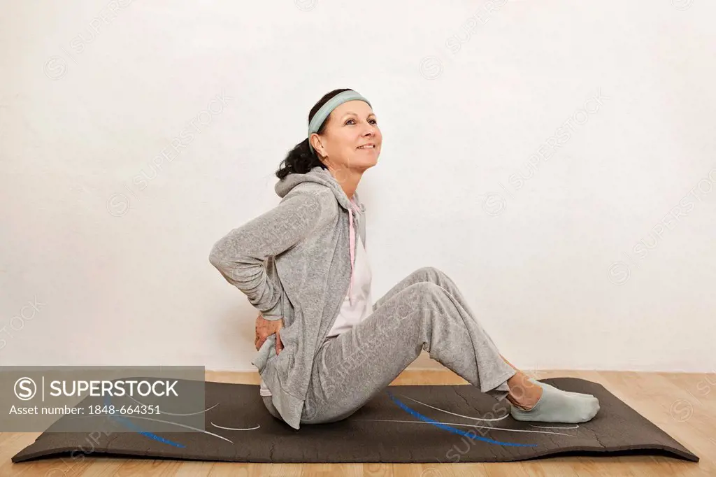 Woman sitting on an exercise mat, doing yoga, exercising to relieve back pain