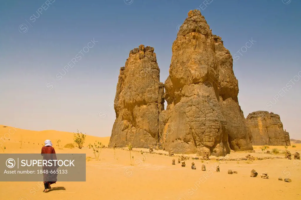 Man walking towards a rock formation in the Sahara Desert, La vache qui pleure, Algeria, Africa