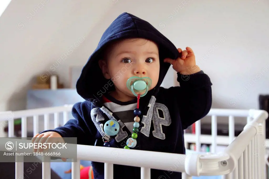 Little boy, 10 months, in the cot with pacifier and hoodie