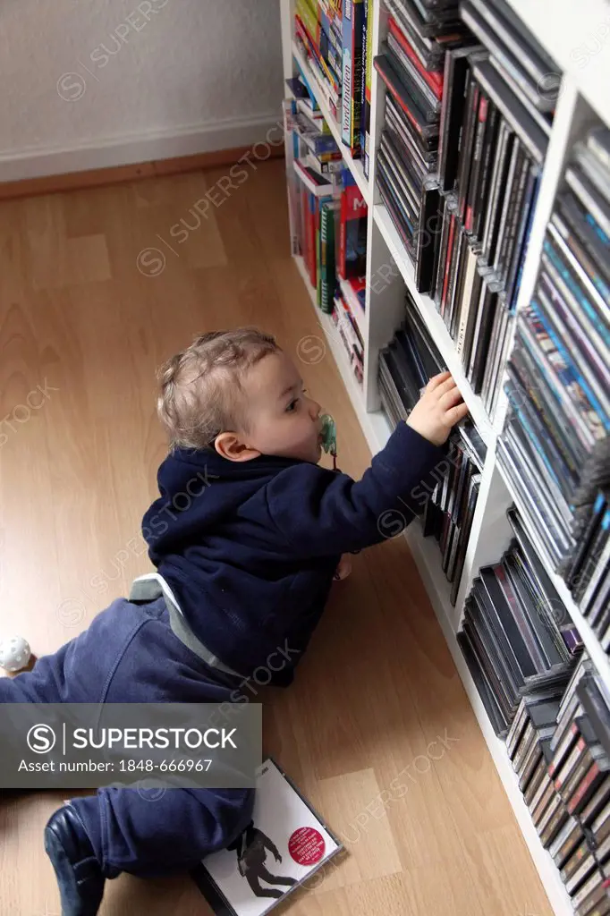 Little boy, 10 months, taking CDs off the shelf