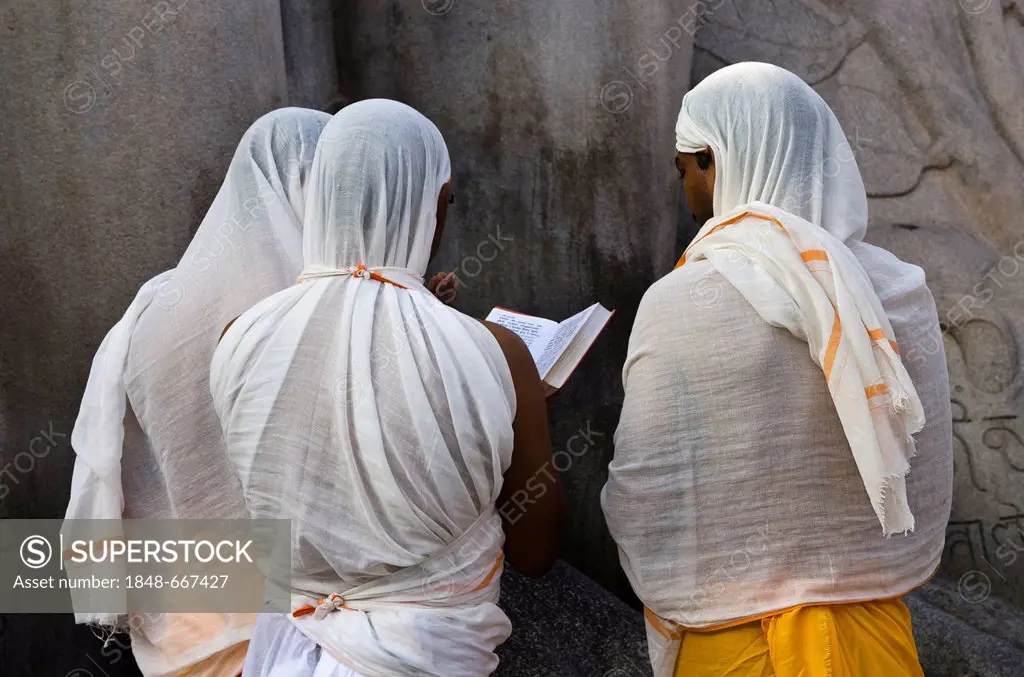 A small group of Jain pilgrims is reciting religious texts at the feet of the statue of Lord Gomateshwara, the tallest monolithic statue in the world,...
