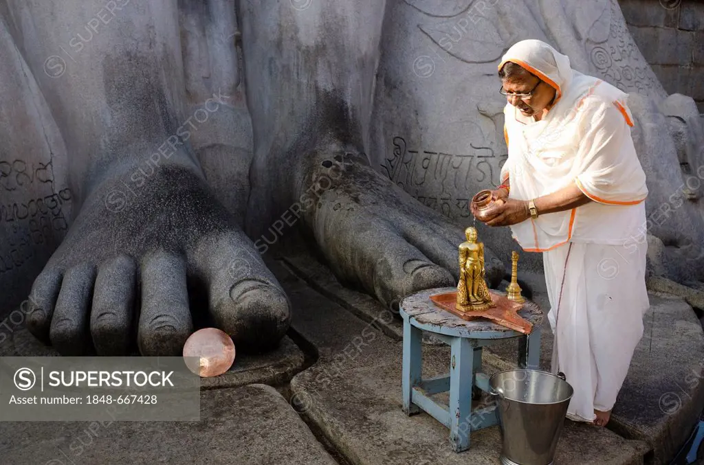 Jain pilgrim is pouring water over a small statue at the feet of the statue of Lord Gomateshwara, the tallest monolithic statue in the world, dedicate...