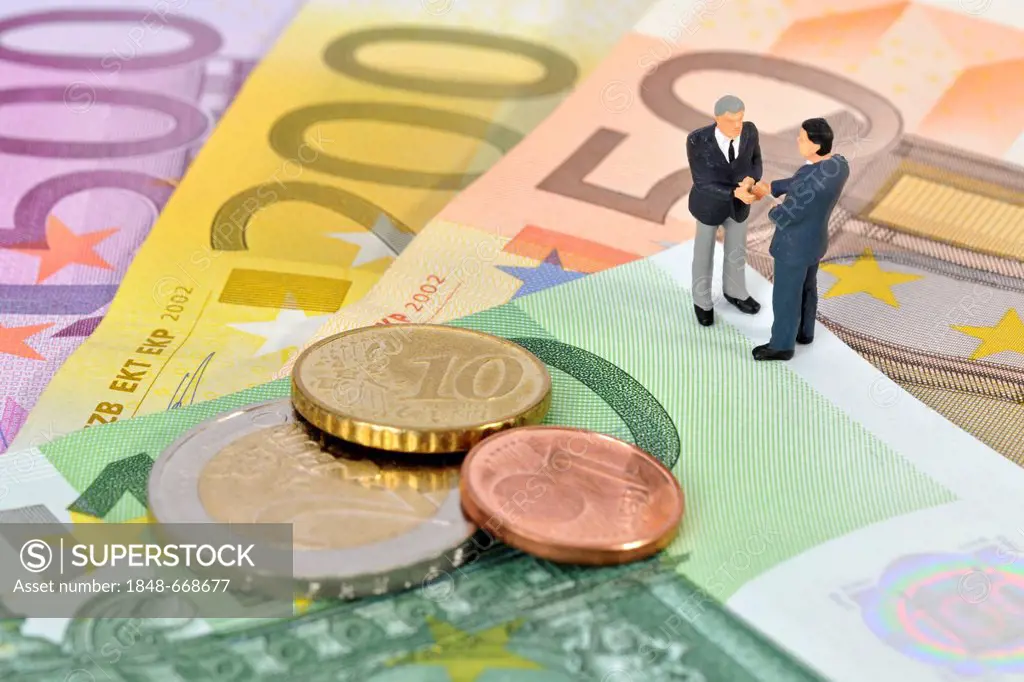Miniature figurines of managers shaking hands while standing on euro banknotes and coins, symbolic image for business, sealing a contract
