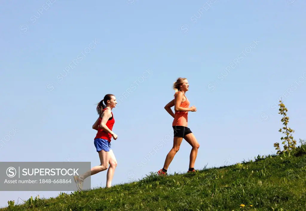 Two recreational runners, young women, 25-30 years, jogging uphill