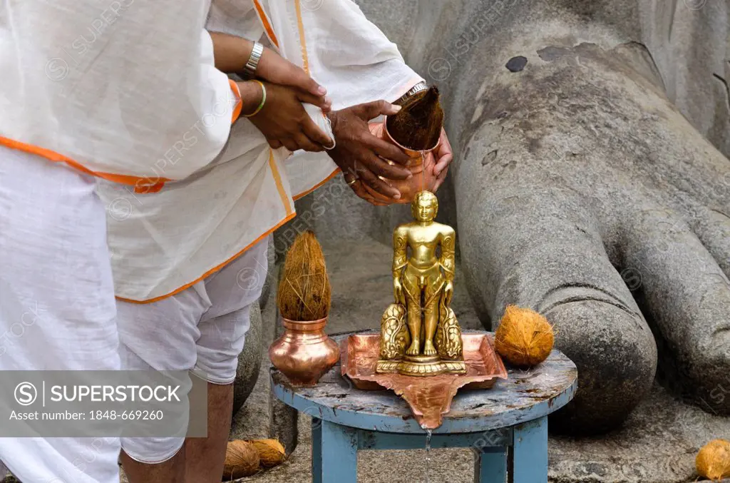 Two Jain pilgrims are pouring water over a small statue at the feet of the statue of Lord Gomateshwara, the tallest monolithic statue in the world, de...