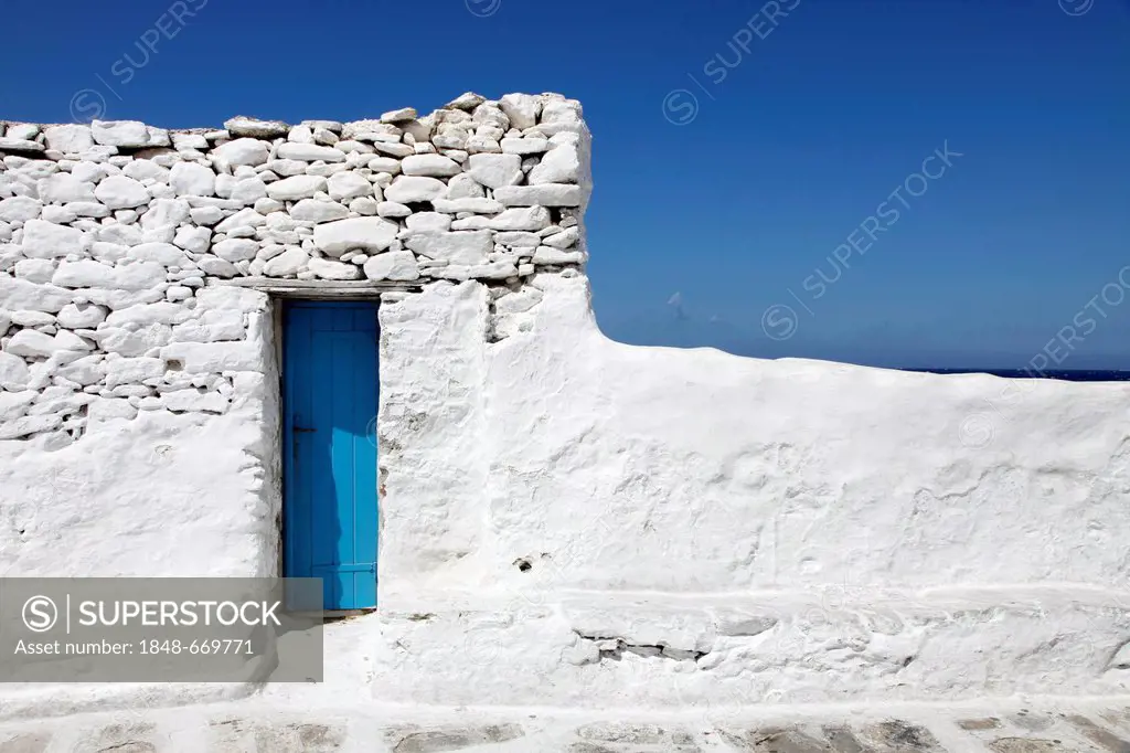 Small narrow blue wooden door in a whitewashed wall of rough stones, Mykonos, Greece, Europe
