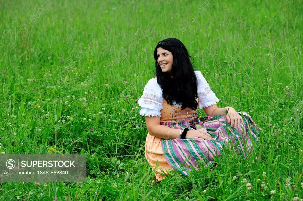Smiling woman wearing a dirndl dress, sitting in a meadow in Tyrol, Austria, Europe