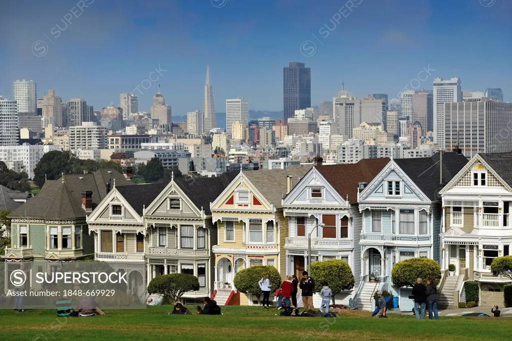 Tourists in front of Painted Ladies, Victorian, multi-coloured painted wooden houses in front of the skyline with the Transamerica Pyramid, Steiner St...