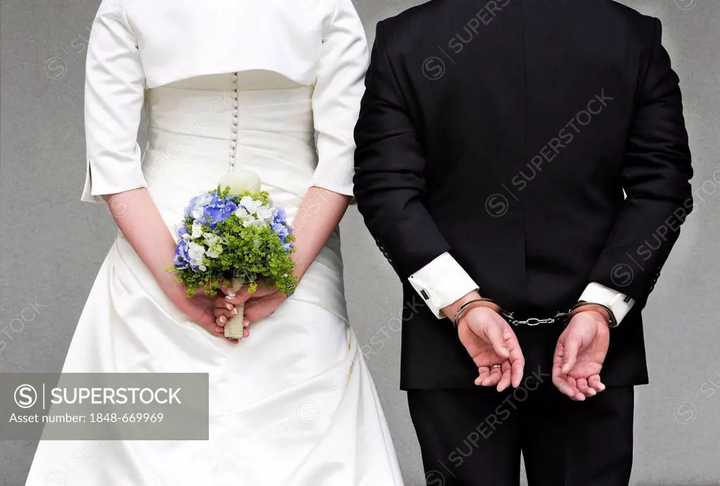 Wedding couple seen from behind, the bride is holding a bridal bouquet, the groom is wearing handcuffs