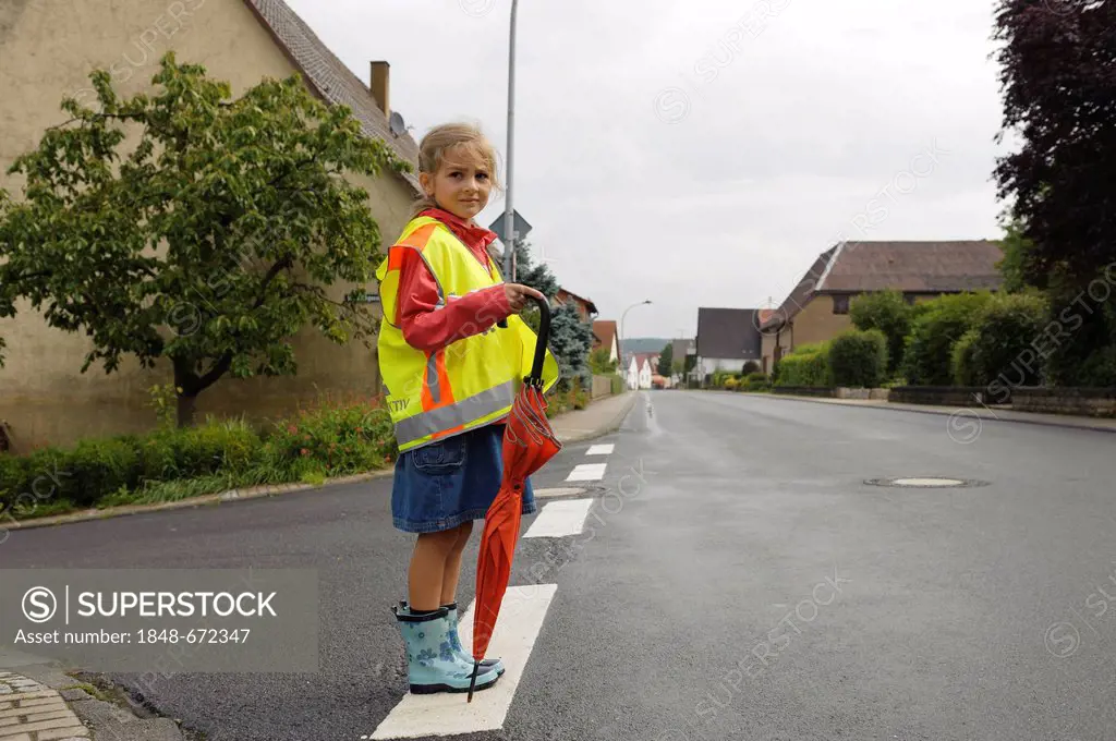 7-year-old girl with yellow safety vest for school children waiting to cross the wet main street, Assamstadt, Baden-Wuerttemberg, Germany, Europe