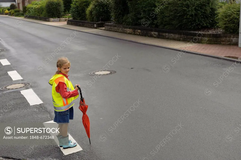 7-year-old girl with yellow safety vest for school children waiting to cross the wet main street, Assamstadt, Baden-Wuerttemberg, Germany, Europe