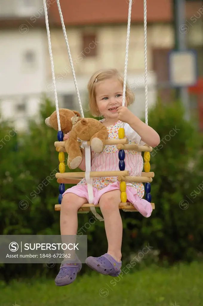 Girl, 2 years, on a swing with a teddy bear