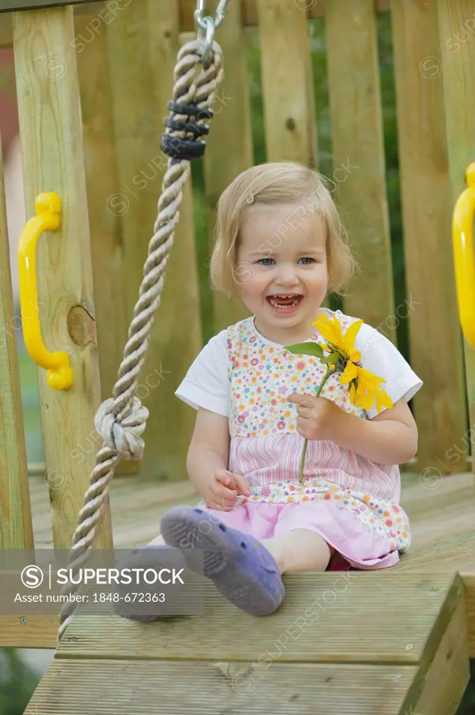 Laughing 2-year-old girl with a sunflower in a play house