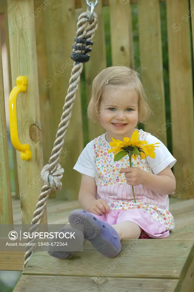 Smiling 2-year-old girl with a sunflower in a play house