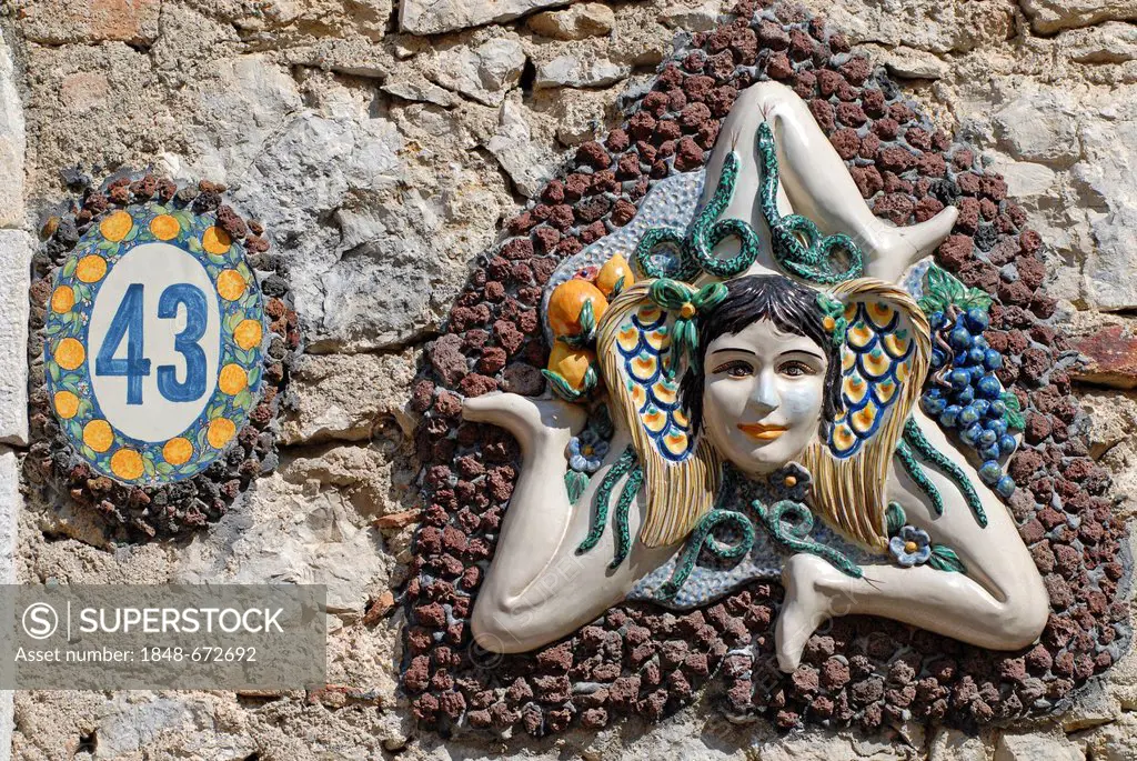 The symbol of Sicily, a girl's head surrounded by snakes and small wings with three running angled legs, sun wheel, on a wall, Taormina, Messina, Sici...
