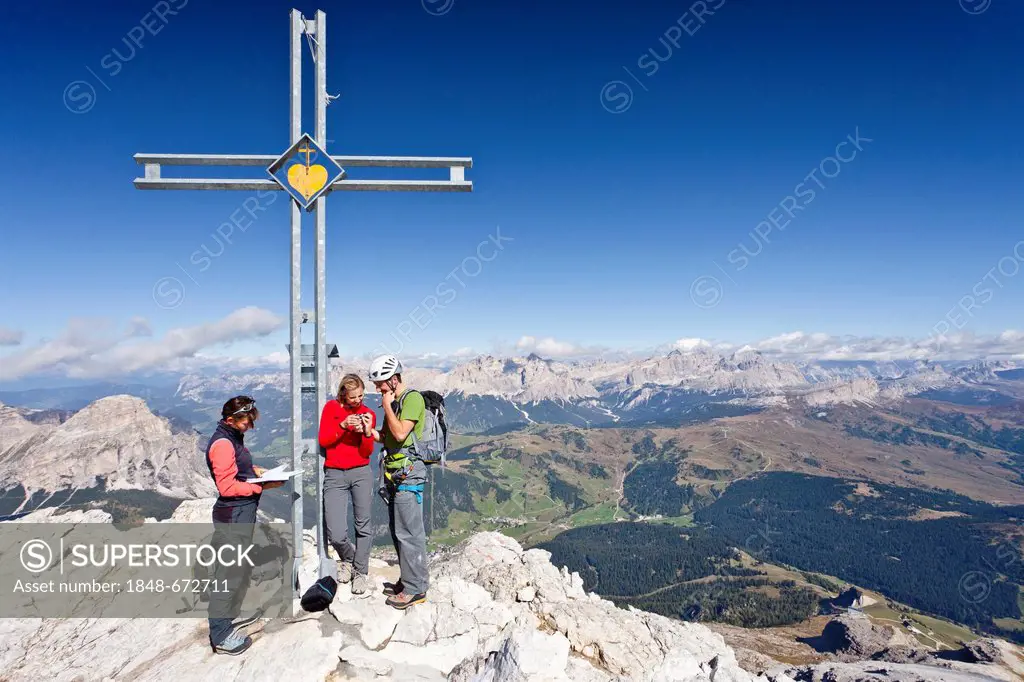 Climbers standing next to the summit cross, Boeseekofel fixed rope route, Dolomites, Fanes group and Heiligkreuzkofel group at the back, province of T...