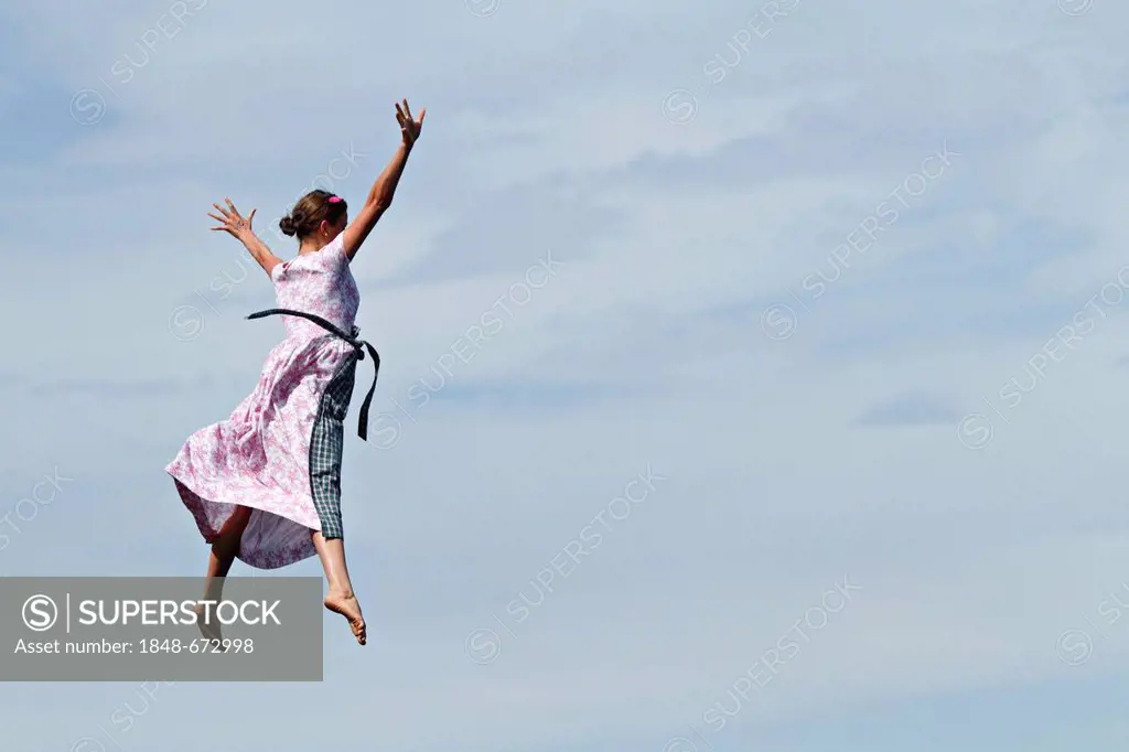 Woman wearing traditional Bavarian dress jumping through the air into Lake Chiemsee at traditional Dirndl-Flugtag, or Dirndl-Flying-Day, Prien Stock, ...