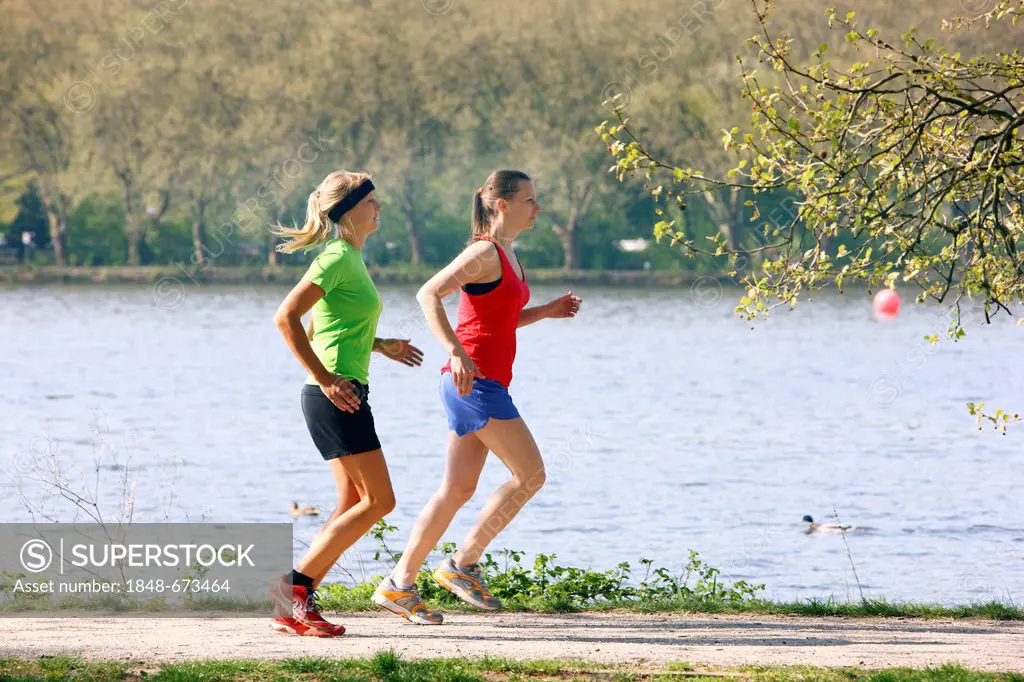 Two recreational runners, young women, 25-30 years, jogging on a lakeside path