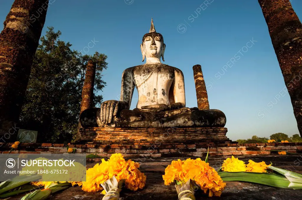 Flowers in front of the seated Buddha statue at Wat Mahathat temple, Sukhothai Historical Park, UNESCO World Heritage Site, Northern Thailand, Thailan...