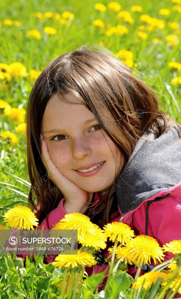 Girl, 12 years, lying in a field of dandelion, smiling