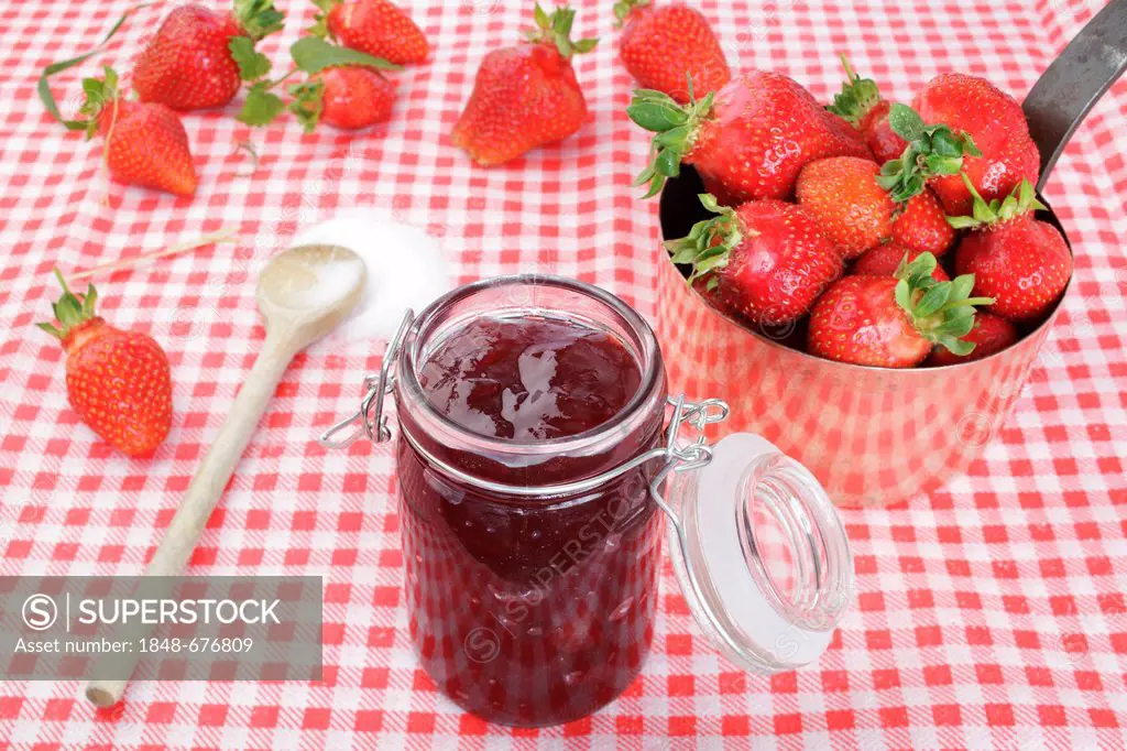 Strawberry jam in a glass, strawberries in a copper pot and sugar on a wooden spoon