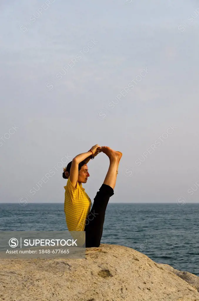 Woman in a yoga position, a variation of Paschimothanasana, by the sea in Kanyakumari, Tamil Nadu, India, Asia