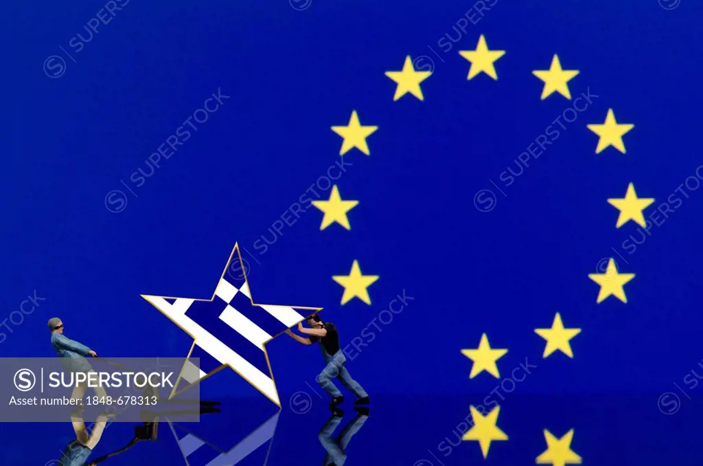 Two miniature warehouse worker figures pushing a star with the Greek flag away from the European flag, symbolic image for the euro crisis