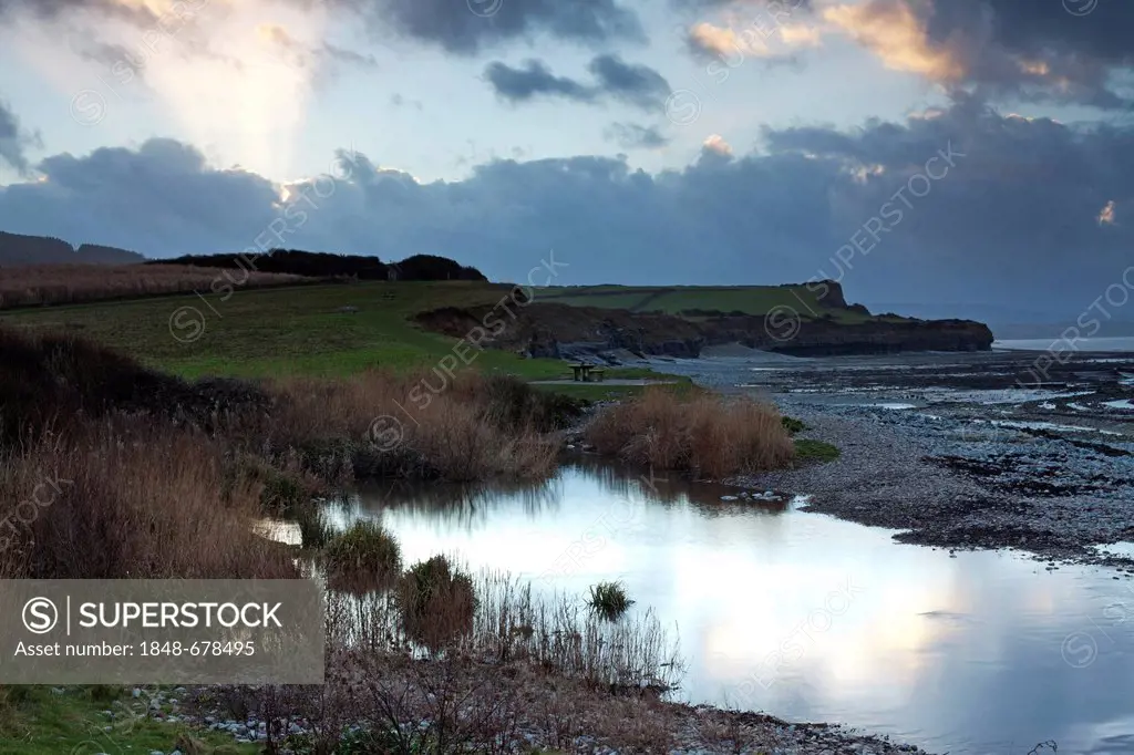 Sunrays through the clouds over the cliffs of Kilve Beach close to sunset, with Kilve Pill or pool of the River Holford in the foreground, Kilve, Some...