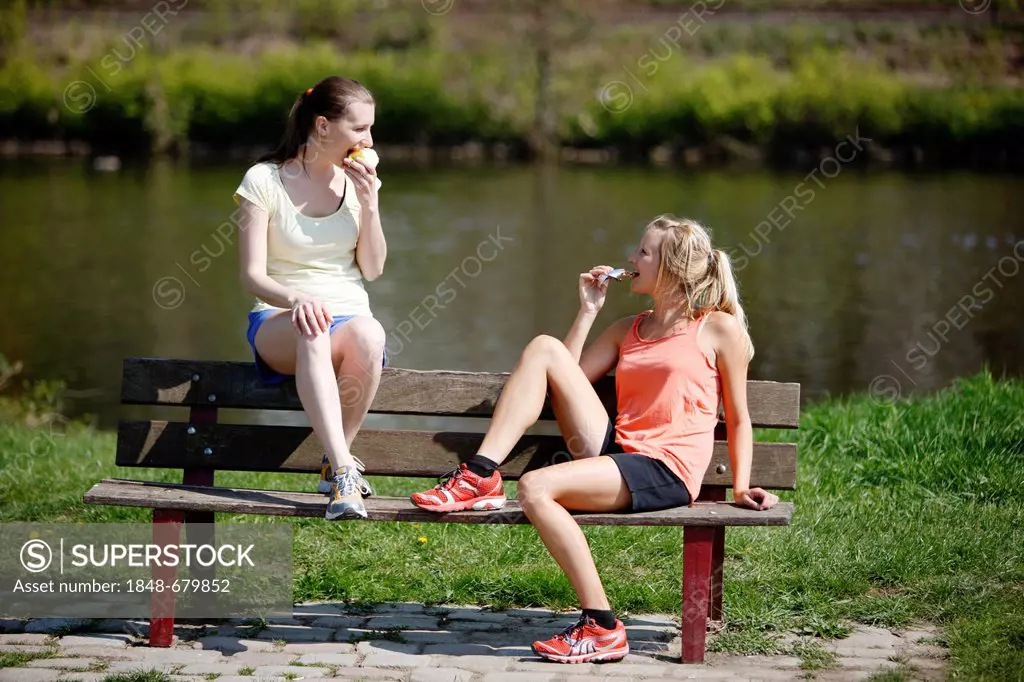 Young women, 25-30 years, eating on a bench after exercise