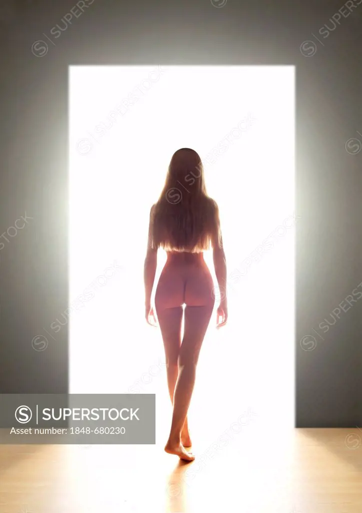 Naked young woman, back view, going through a door into the light