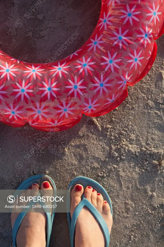Feet in flip-flops on the beach with swim ring