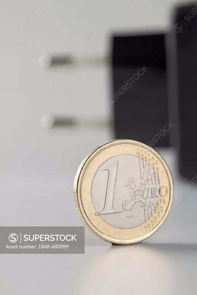 One-euro-coin and a power plug at the back, symbolic image for electricity rates