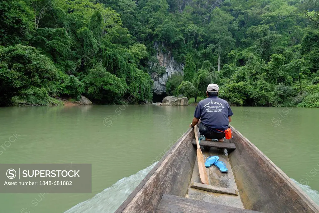 Laotian man with a simple long boat at the entrance of the 7.5 km long cave of Tham Kong Lor, in the dense tropical rain forest, Khammouane, Laos, Sou...