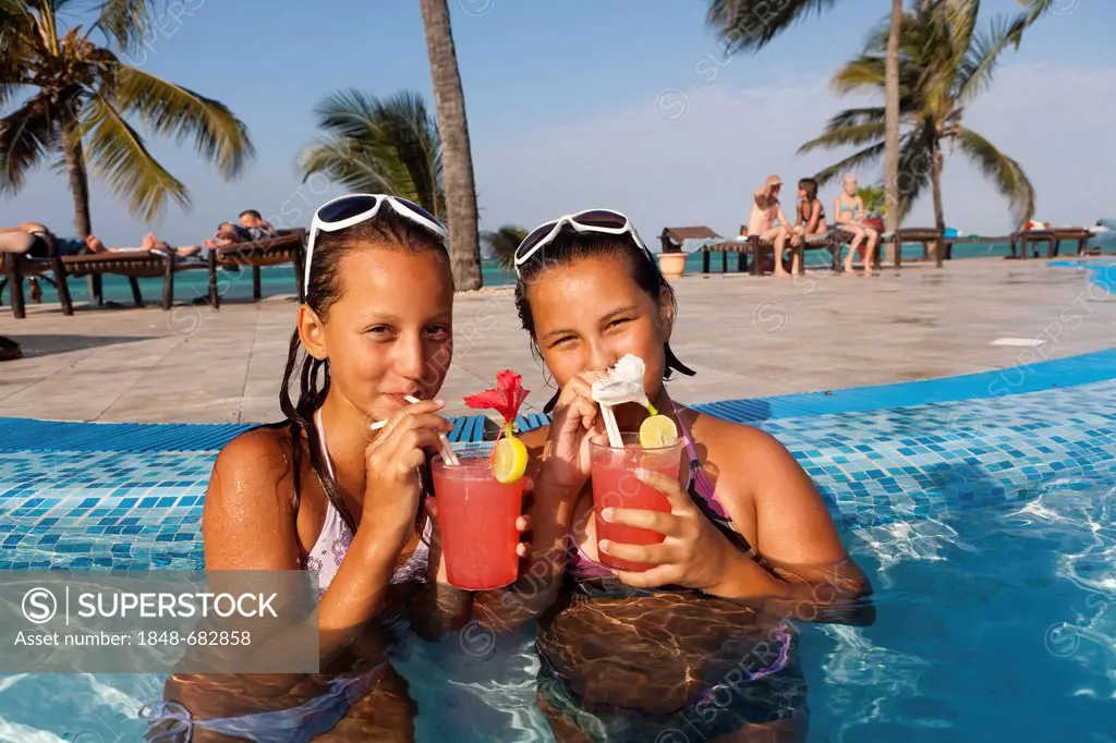 Two girls with sunglasses, about 12 years, drinking cocktails in a swimming pool