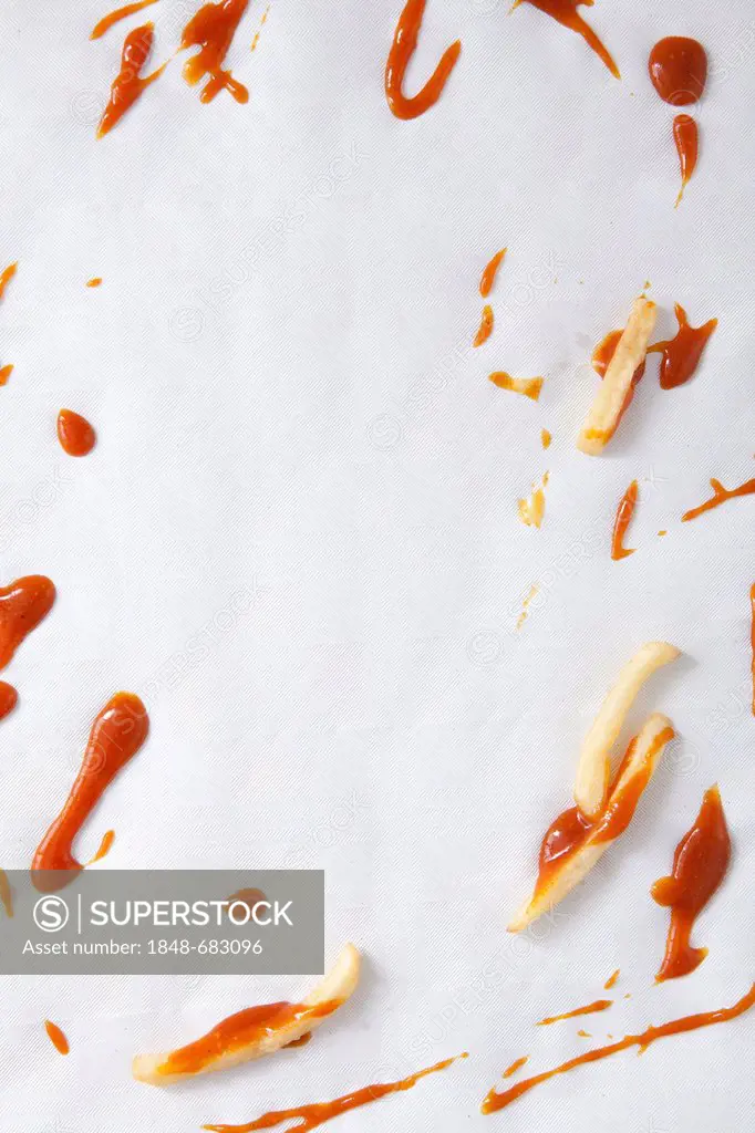 French fries and spilled ketchup on a paper table cloth, food scraps