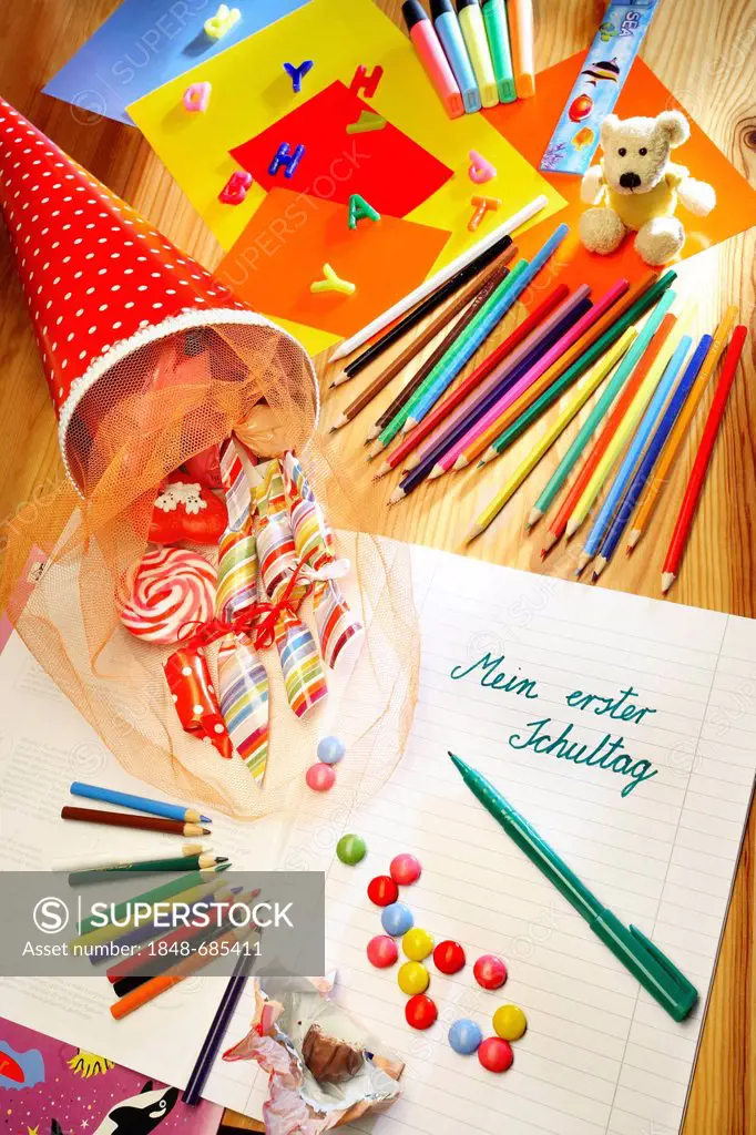 Schultuete or school cone filled with gifts and sweets beside coloured pencils and a notebook with the heading Mein erster Schultag, German for My fir...