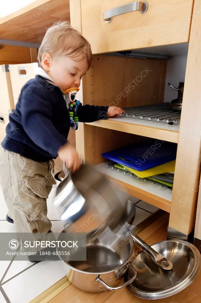 Little boy, 10 months, taking cooking pots from a cupboard in the kitchen