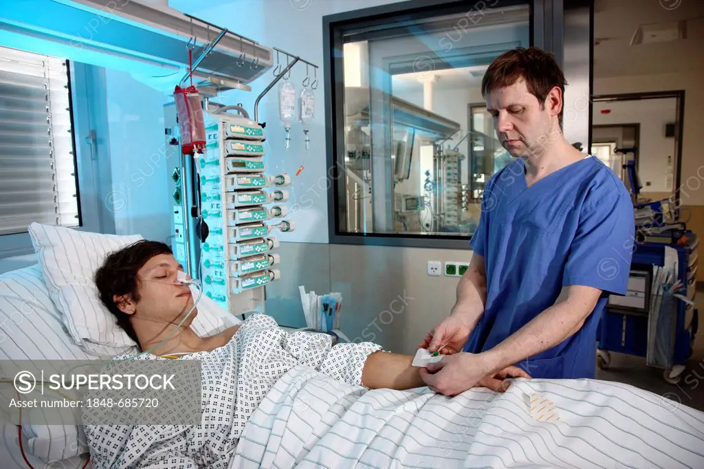 Male intensive care nurse looking after a patient lying in a special bed, medical treatment and artificial respiration of the patient, automatic monit...