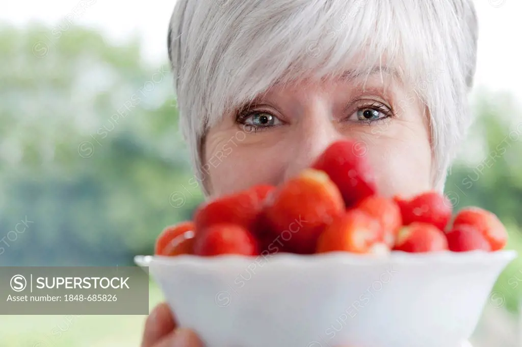 Woman's face behind a bowl of fresh strawberries