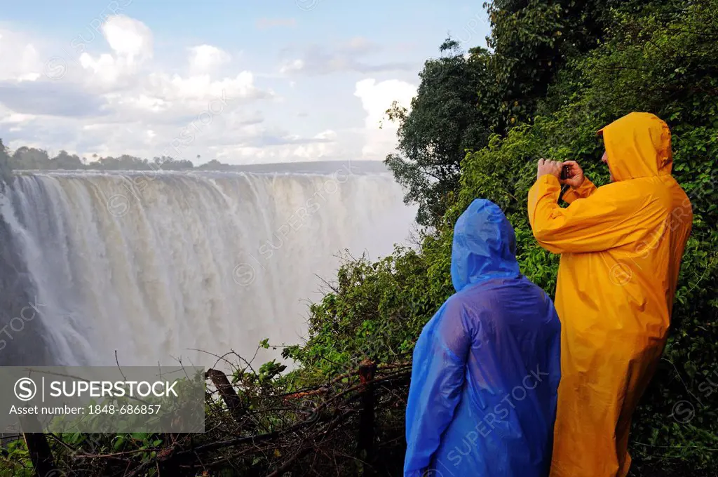 Tourists in rain jackets photographing the Victoria Falls, waterfall on the Zimbabwean side of the river Zambezi, Victoria Falls town, Zimbabwe, Afric...