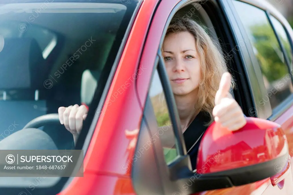 Young woman looking out the window of a car with her thumb up