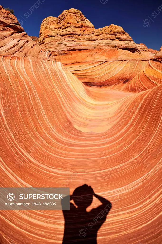 Shadow of a photographer on The Wave, banded eroded Navajo sandstone rocks with Liesegang Bands, Liesegangen Rings, or Liesegang Rings, North Coyote B...