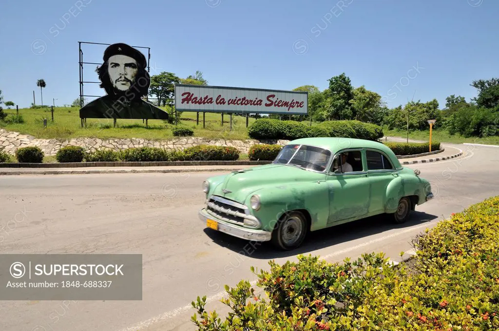 Vintage car in front of revolutionary propaganda, Hasta la victoria siempre, Spanish for ever onward to victory with portrait of Ernesto Che Guevara, ...