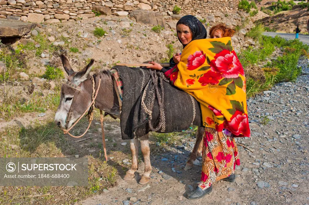 Young mother travelling with a donkey and carrying her infant in a sling on her back, High Atlas Mountains, Morocco, Africa