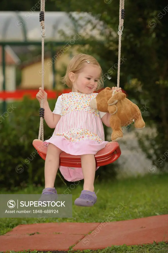 Girl, 2 years, on a swing with a teddy bear