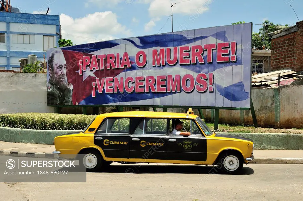 Stretched Lada taxi in front of an advertising panel with political propaganda on it, Fidel Castro, Socialismo o muerte, socialism or death, Bayamo, C...