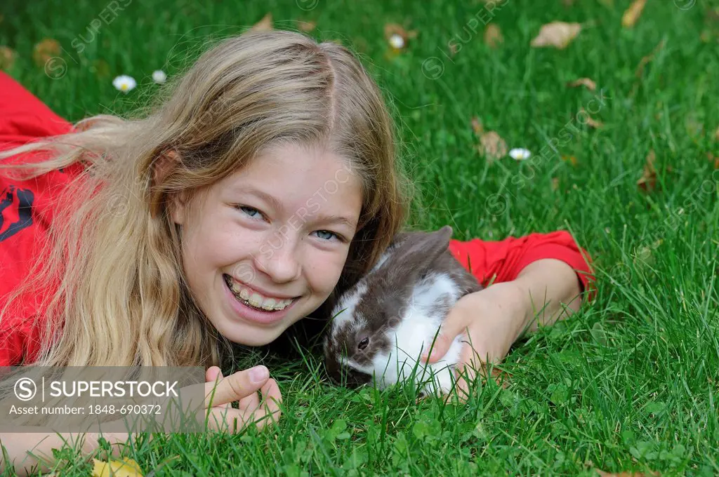 Girl, 11, cuddling with a young Domestic Rabbit (Oryctolagus cuniculus forma domestica) on a meadow