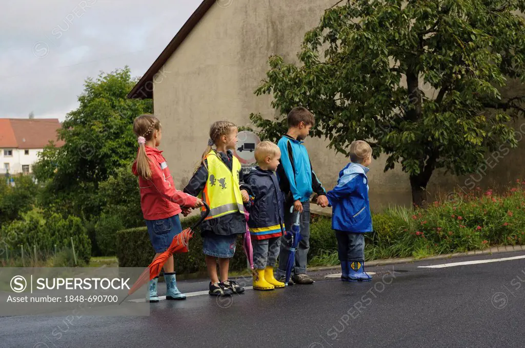 Five children crossing a street in the rain, Assamstadt, Baden-Wuerttemberg, Germany, Europe