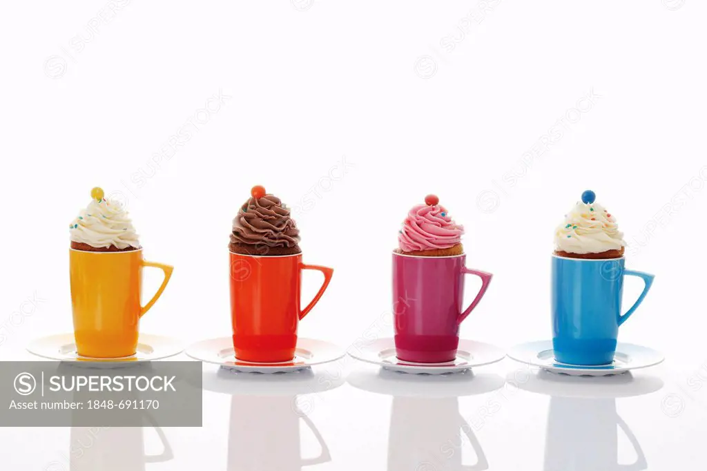 Various cupcakes in colourful coffee mugs, side by side