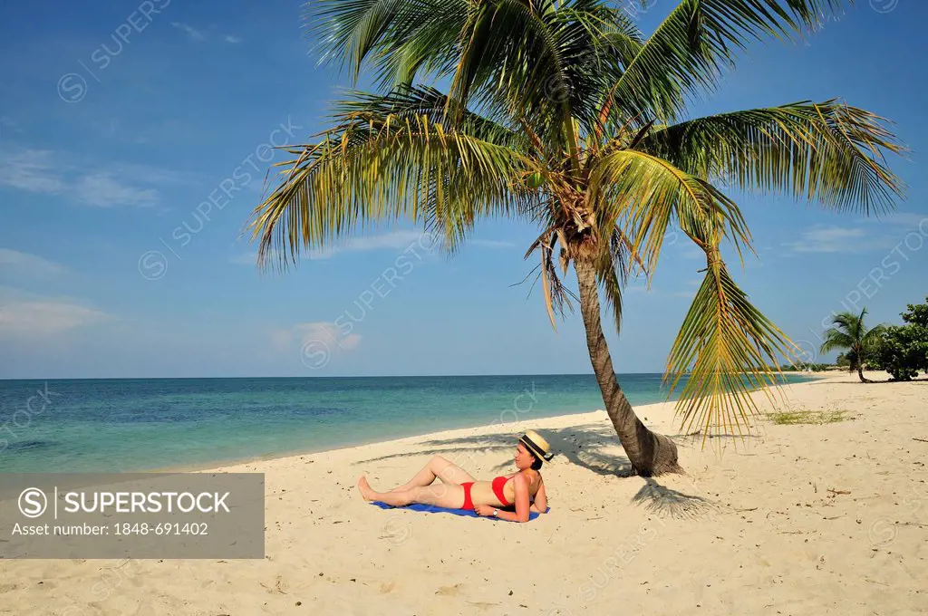 Tourist under a palm tree on the beach, Playa Ancon beach, near Trinidad, Cuba, Caribbean